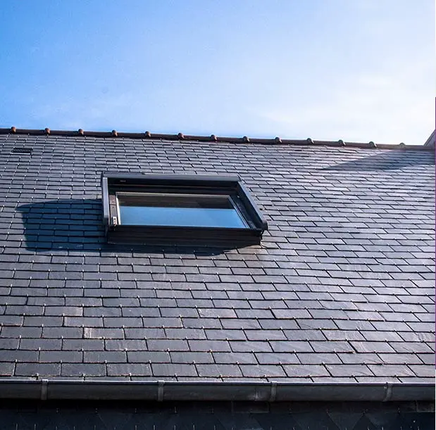 Une toiture en ardoise sombre avec un velux installé, permettant l'entrée de lumière naturelle. Les tuiles sont alignées proprement, assurant une finition soignée et uniforme